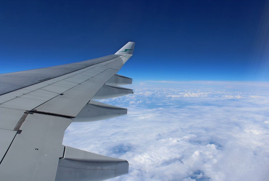 Airplane wing in flight over a cloudscape with clear blue sky
