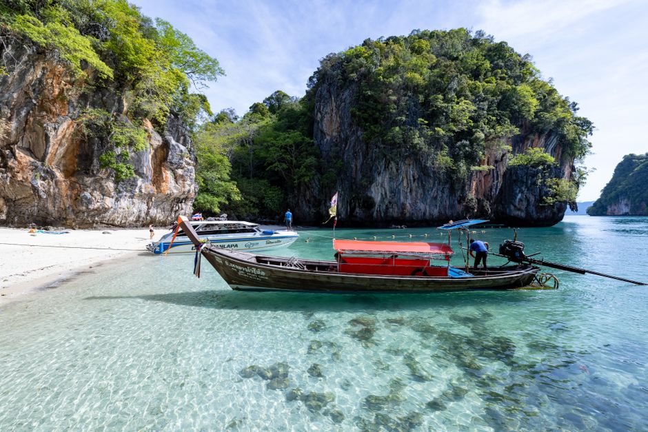 Peaceful Thai beach with clear waters, a longtail boat and limestone cliffs